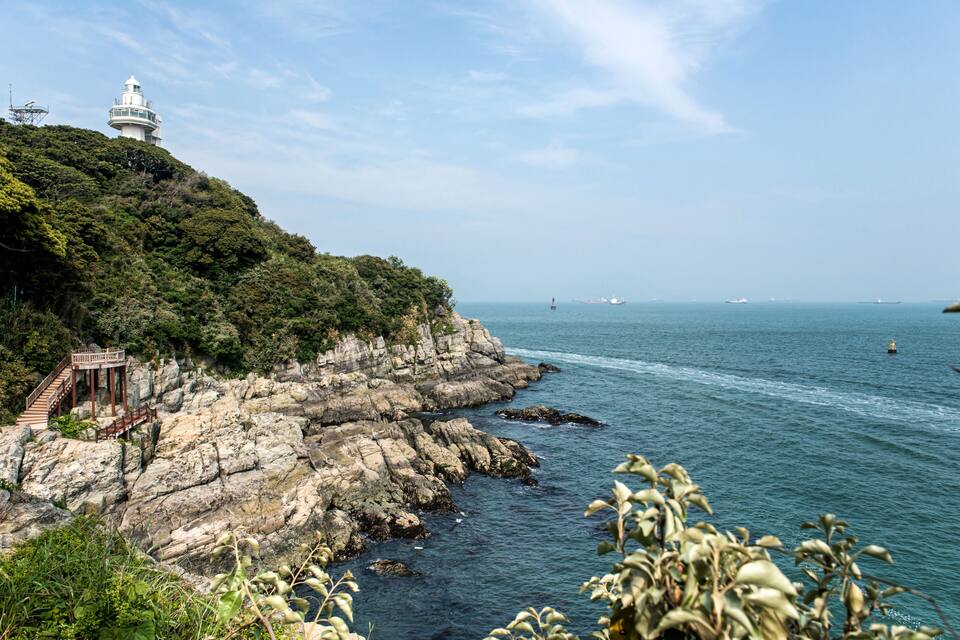 A coastal landscape with a lighthouse, rocky cliffs, and a clear view of the sea.