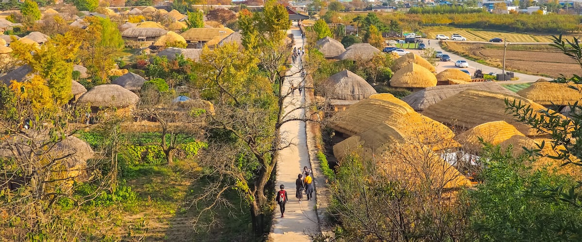 A rural landscape with thatched-roof houses, a winding path, and mountains in the background.