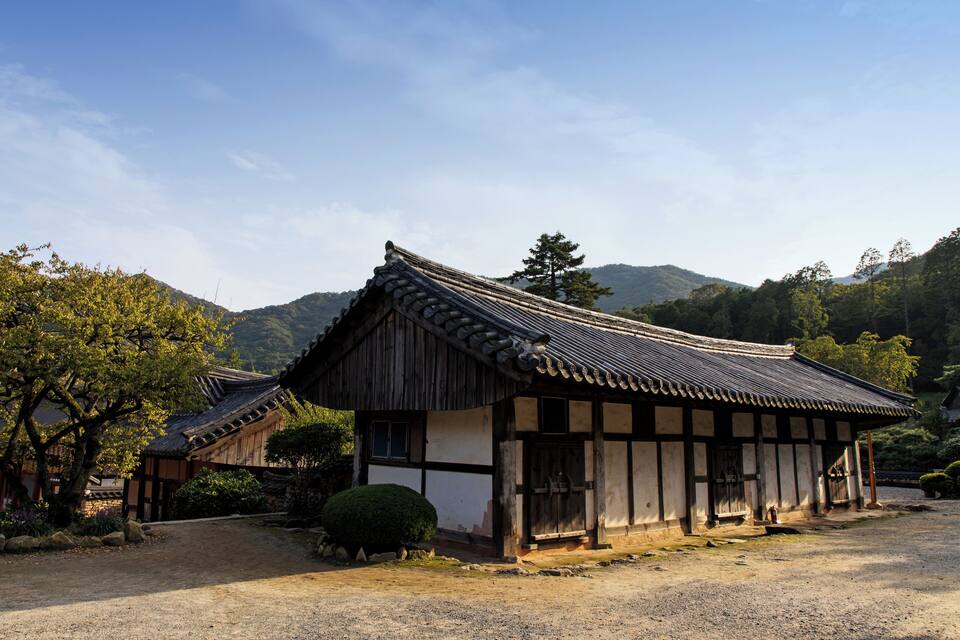 A traditional Korean building with a tiled roof, surrounded by a gravel path and lush greenery.