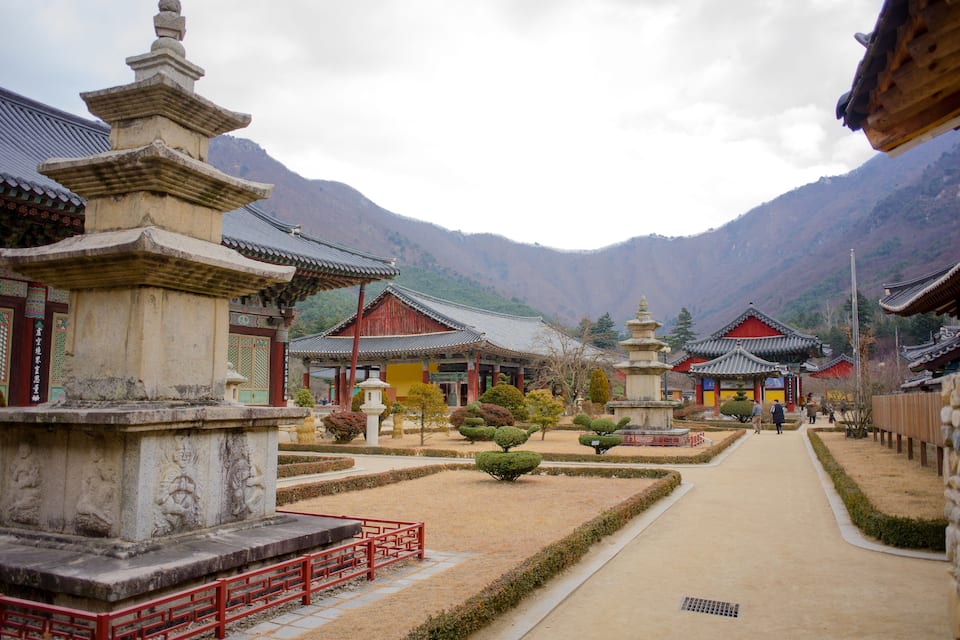A traditional temple complex with tiered pagodas, a central walkway, and mountainous backdrop.