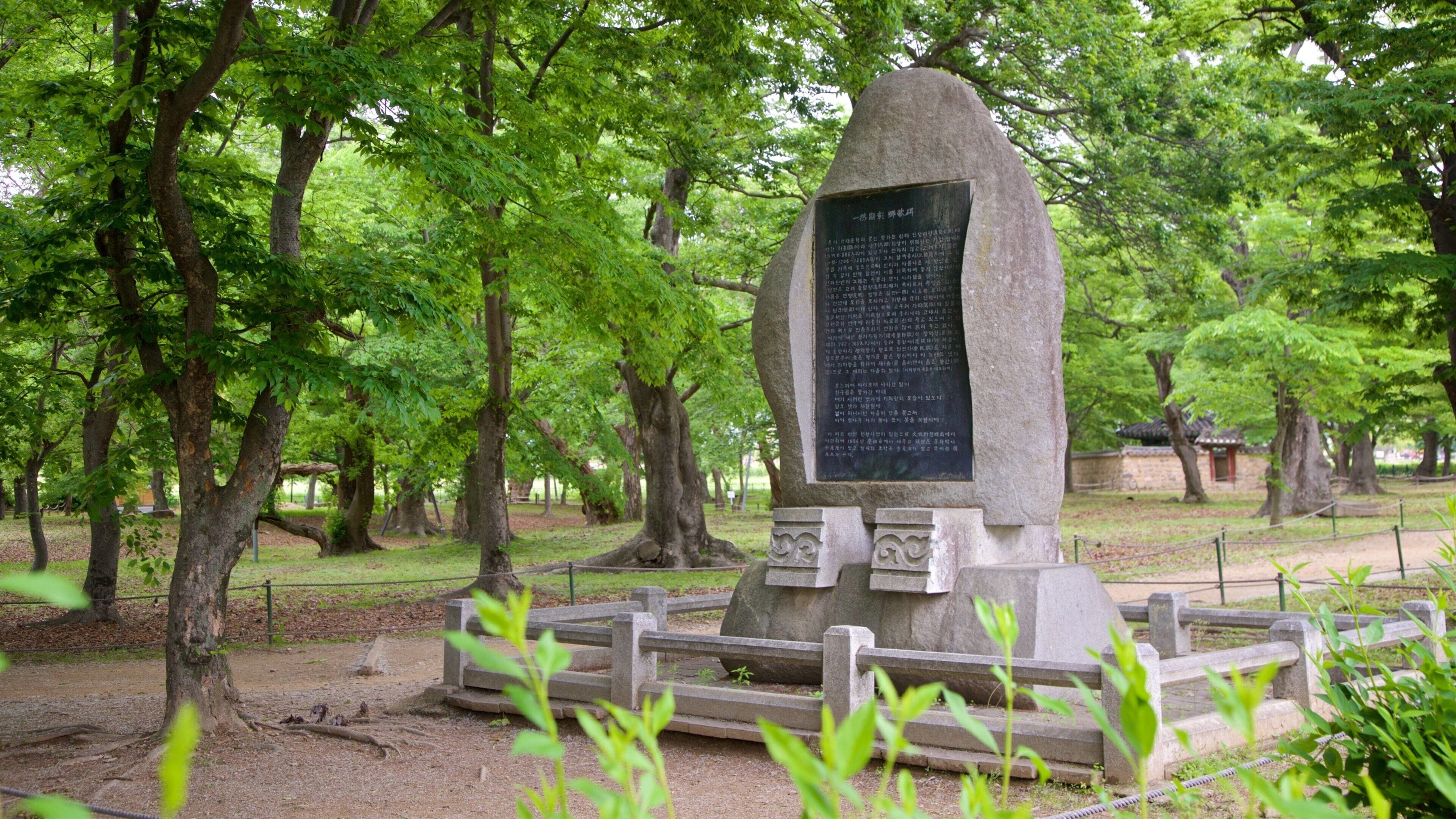 A stone monument with an inscription surrounded by trees in a park.