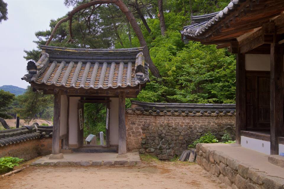 A traditional Korean pavilion with tiled roofs, surrounded by stone walls and lush greenery.