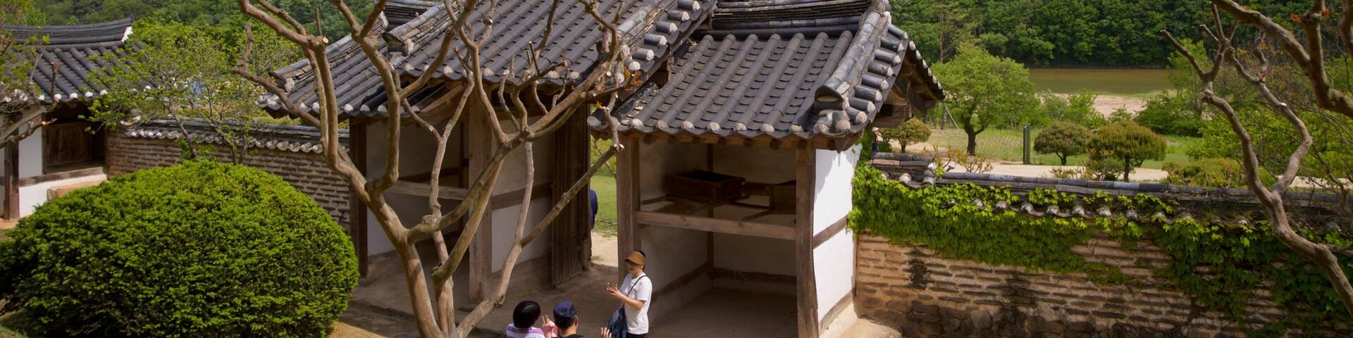 Arquitectura coreana tradicional con tejados de tejas, rodeada de exuberante vegetación y montañas.