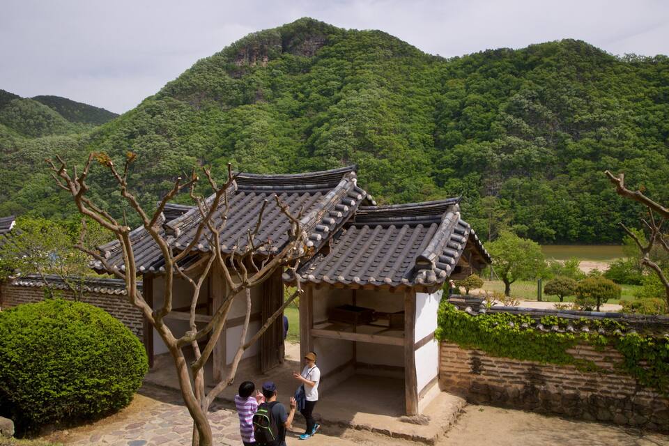Traditional Korean architecture with tiled roofs, surrounded by lush greenery and mountains.