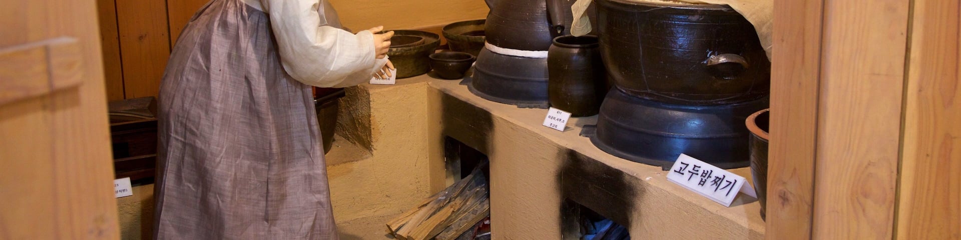 A person in traditional attire examining pottery items in a wooden room with shelves.
