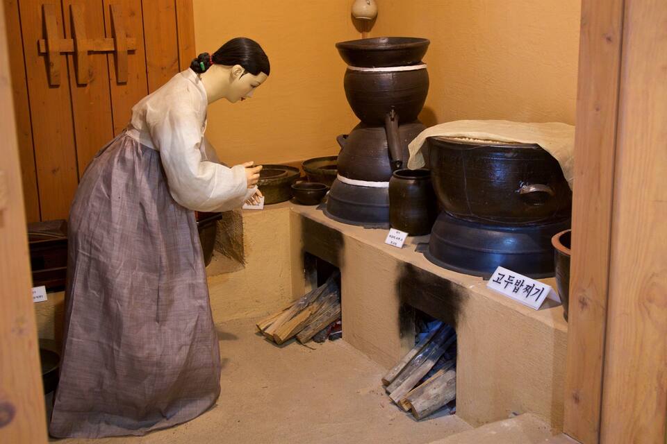 A person in traditional attire examining pottery items in a wooden room with shelves.
