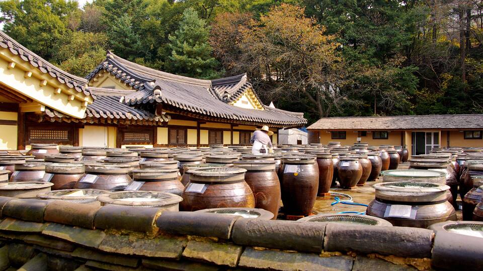 Un templo coreano tradicional con grandes jarrones de cerámica y una persona vestida con atuendo tradicional.