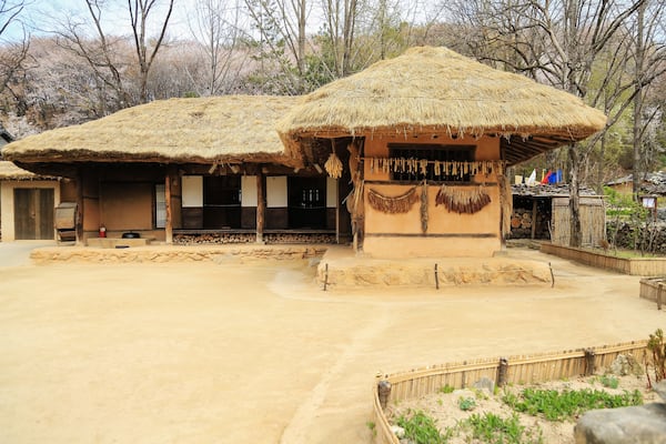 Traditional thatched-roof huts, a sandy courtyard, and a backdrop of leafless trees.