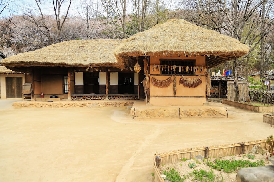 Traditional thatched-roof huts, a sandy courtyard, and a backdrop of leafless trees.