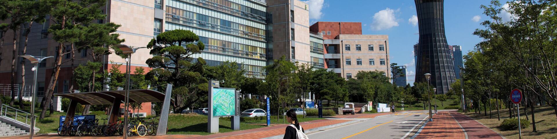 A modern city street with a pedestrian walkway, a tall building, and a unique cylindrical structure.