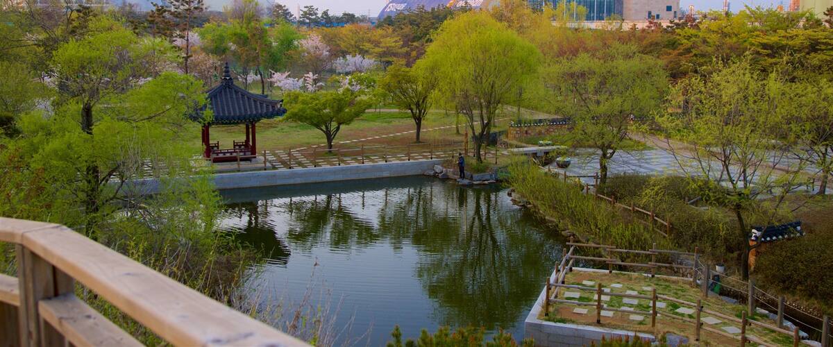 A park with a traditional pavilion, a pond, and modern buildings in the background.