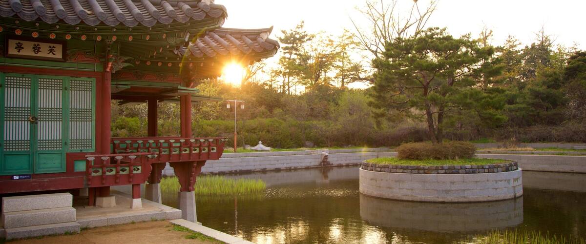 A traditional Korean pavilion with a tiled roof, a stone bridge, and a pond surrounded by trees.