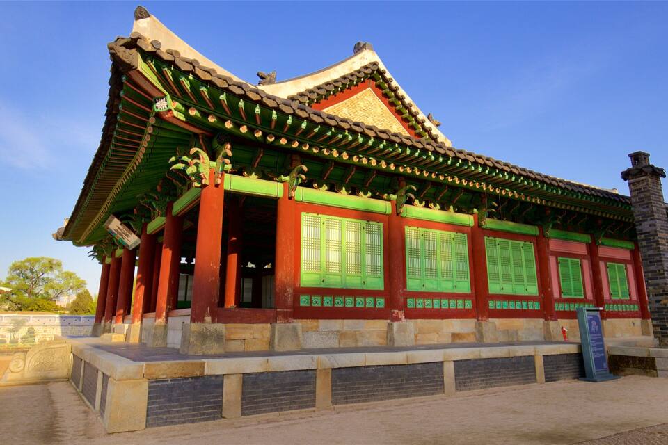 Un bâtiment traditionnel coréen, avec une structure en bois peinte en vert et en rouge, un toit recouvert de tuiles et des marches en pierre menant à l’entrée.