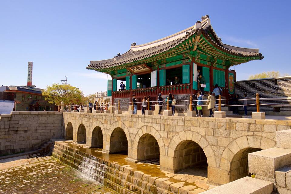 Un pavillon coréen traditionnel aux couleurs verte et blanche, un pont de pierre avec des arches et un petit élément décoratif aquatique.