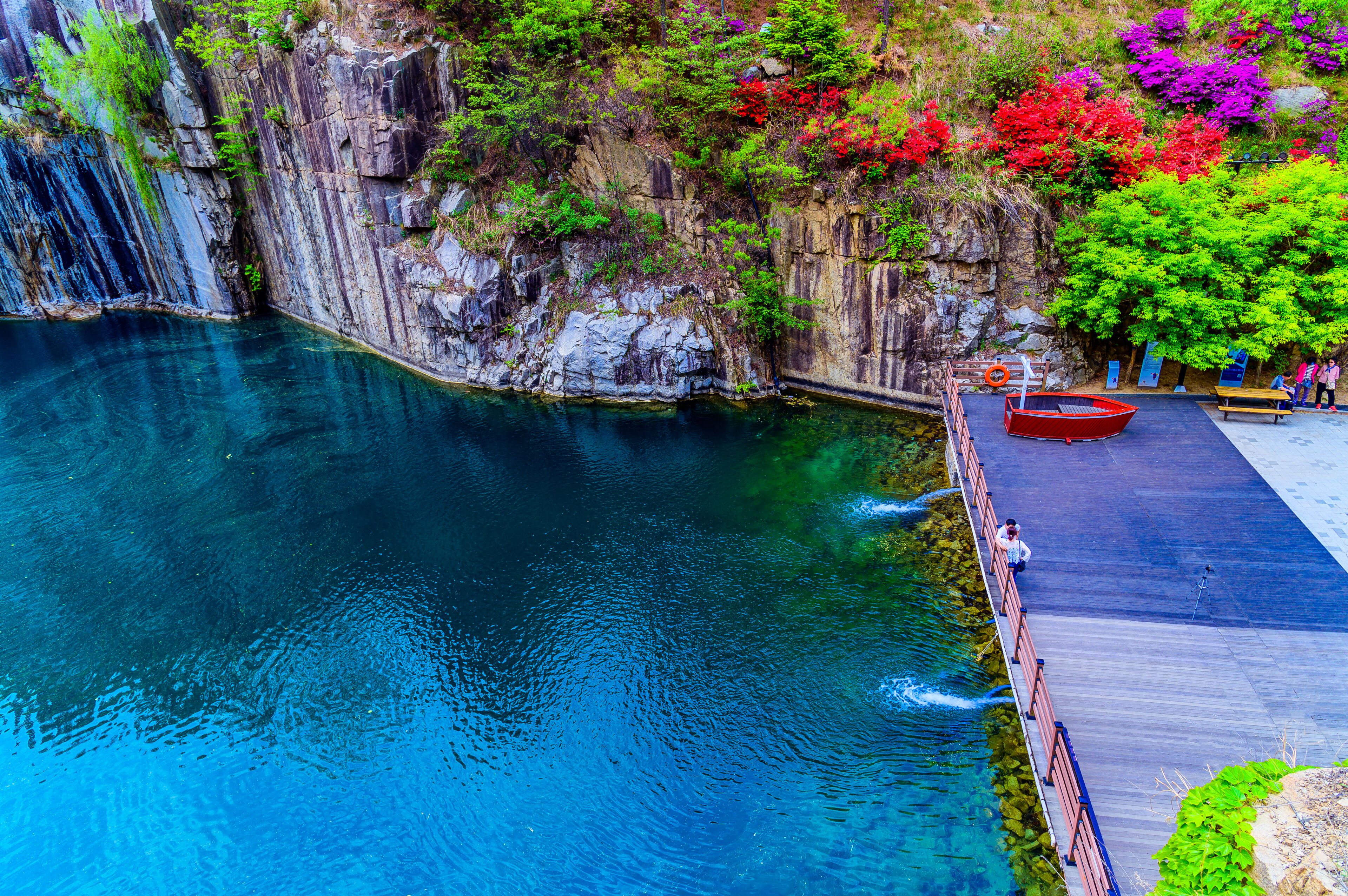 A clear blue water body, a wooden dock, and a red boat.