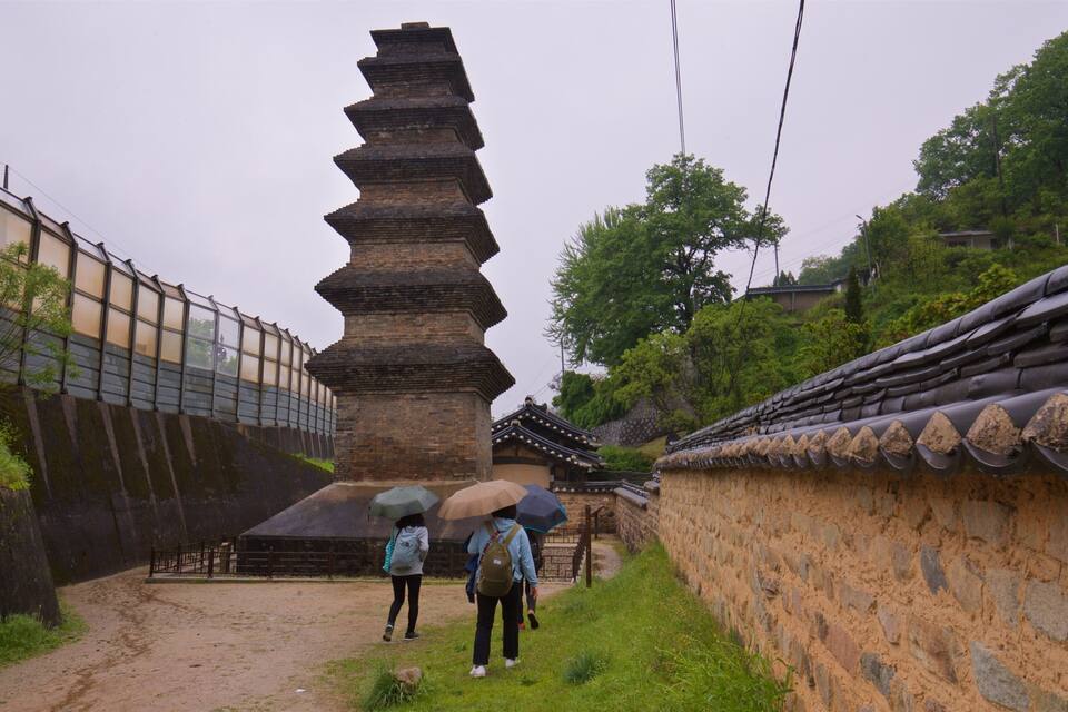 A traditional pagoda with a unique tiered design, surrounded by a stone wall and a wooden fence.