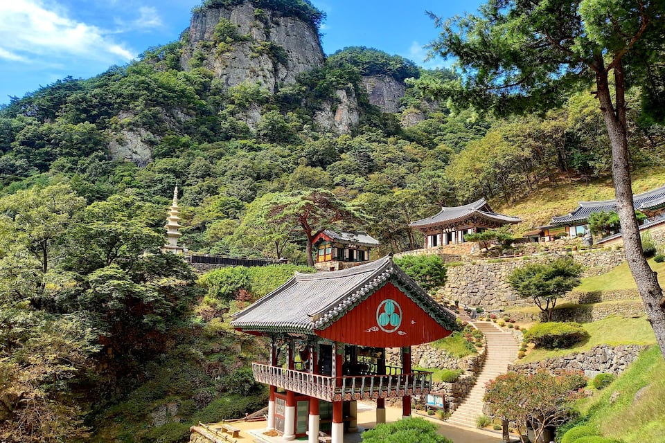 Un complejo tradicional de templos coreanos con una pagoda destacada, exuberante vegetación y montañas rocosas al fondo.