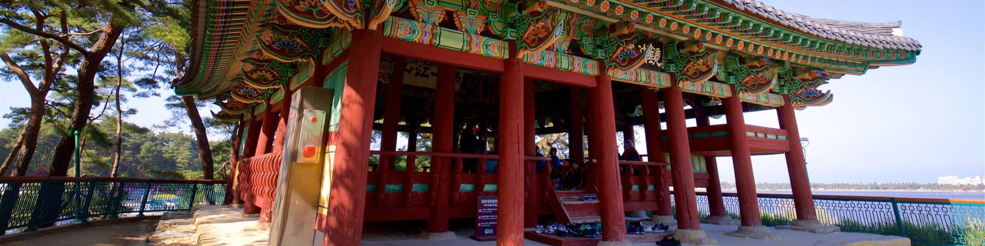 A traditional Korean pavilion with ornate roof tiles and vibrant colors, surrounded by trees and a clear sky.