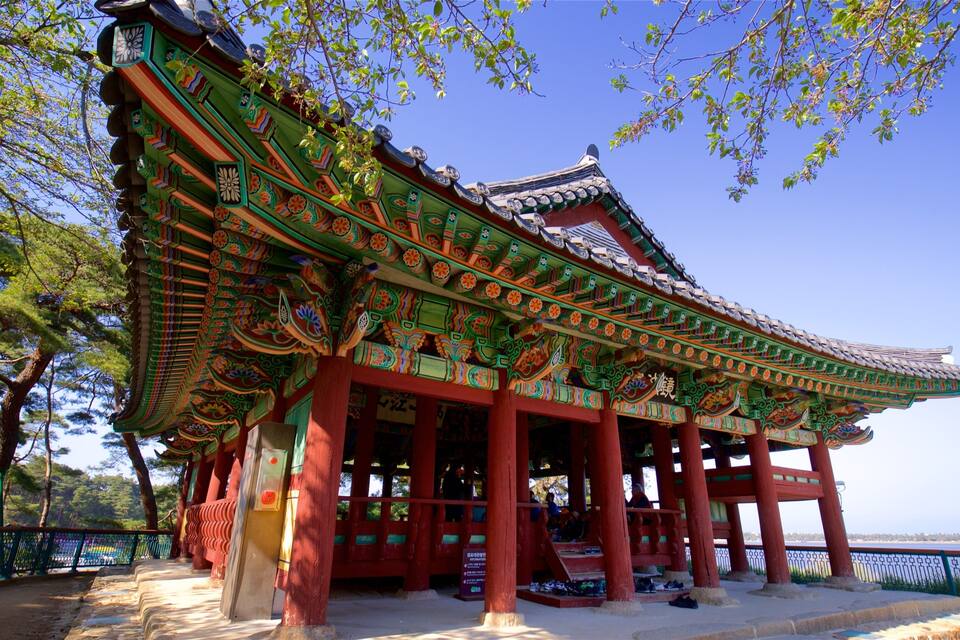 A traditional Korean pavilion with ornate roof tiles and vibrant colors, surrounded by trees and a clear sky.