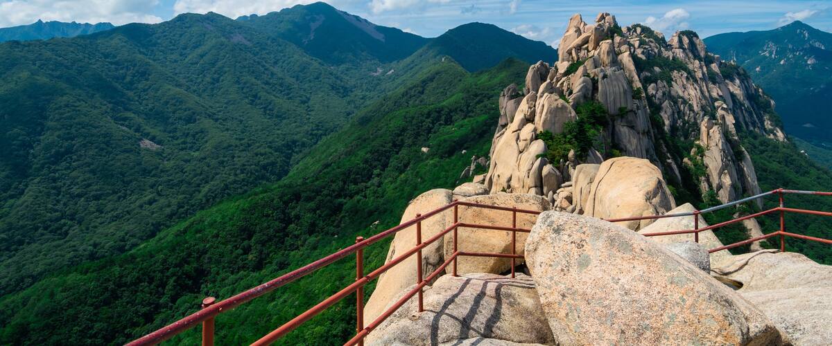A mountainous landscape with a prominent rock formation and a red metal staircase.