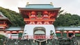 Un templo japonés tradicional con una estructura destacada de rojo y blanco, rodeado de exuberante vegetación y terreno rocoso.