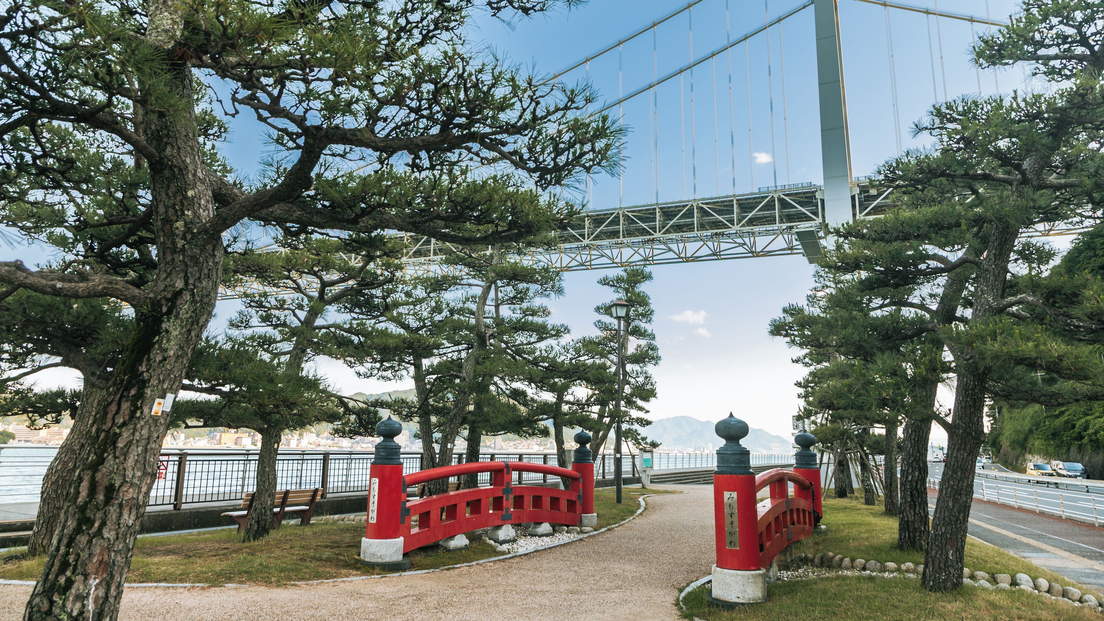Un puente rojo, árboles, un sendero y un río.