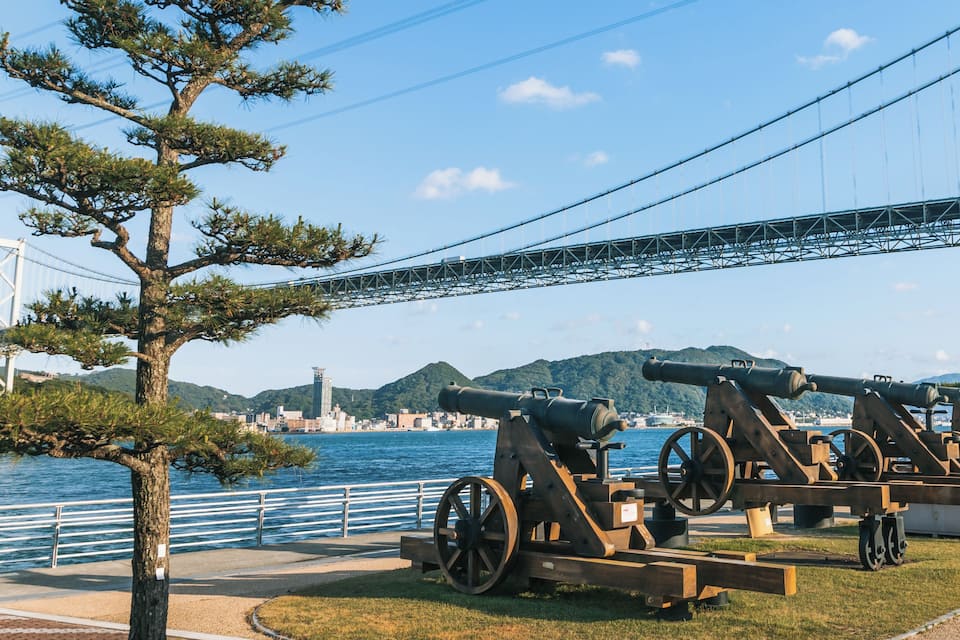 Una ciudad costera con un puente, cañones y un árbol.