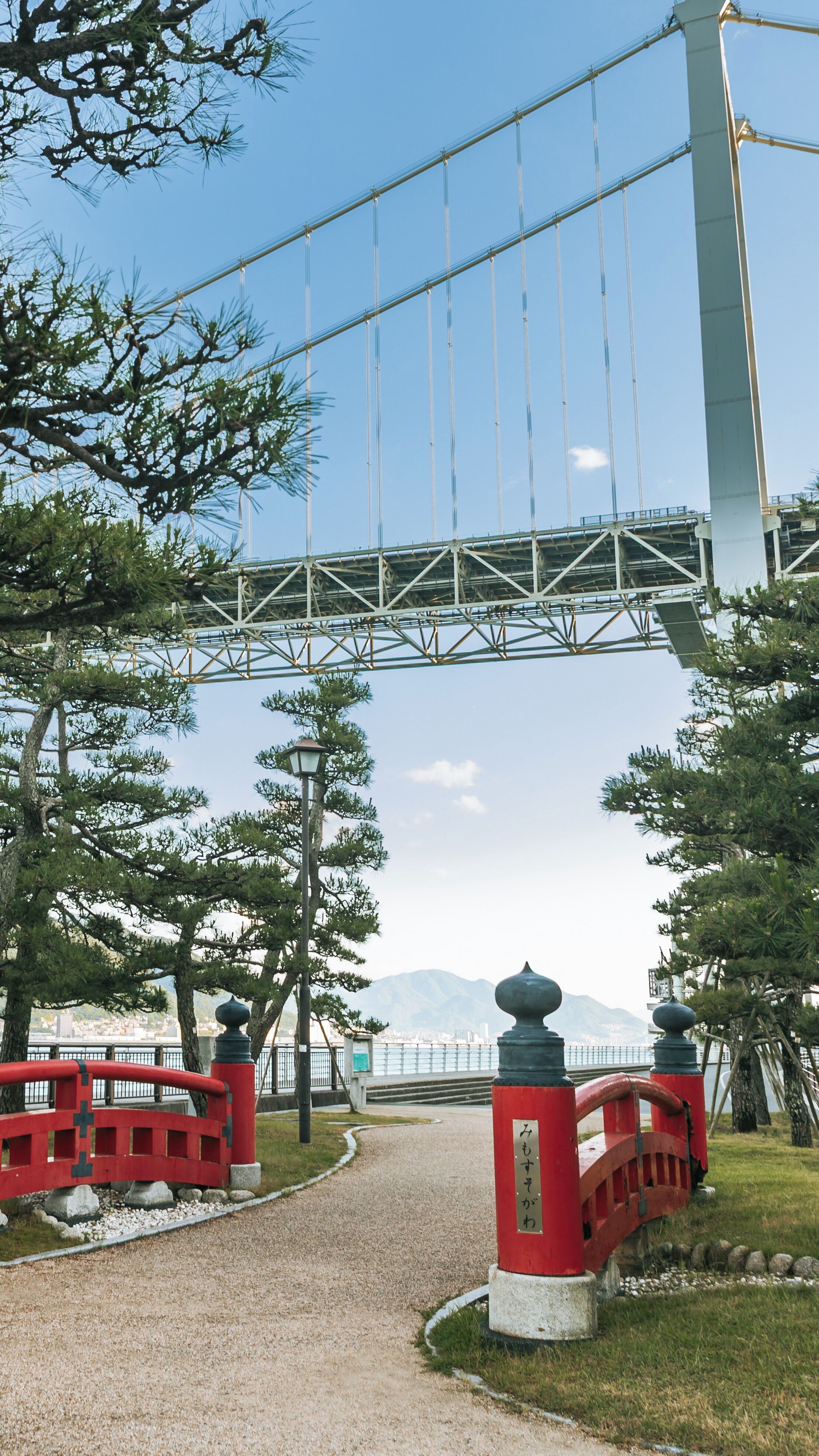 Un puente, un torii rojo y un camino que lleva a una masa de agua.