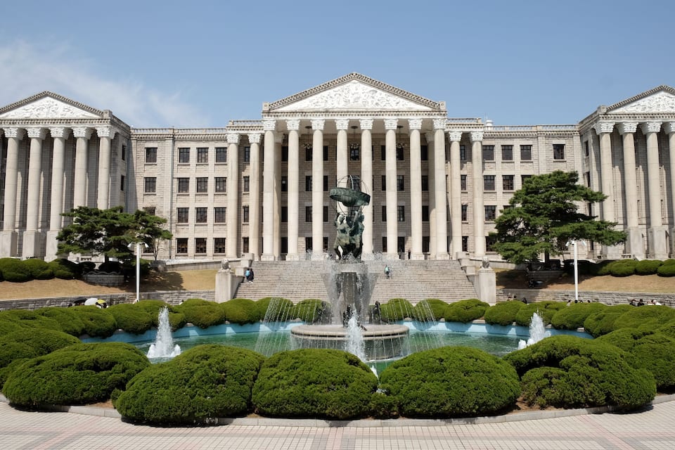 Ein prachtvolles Gebäude mit Säulen und einem zentralen Brunnen, umgeben von gepflegten Büschen.