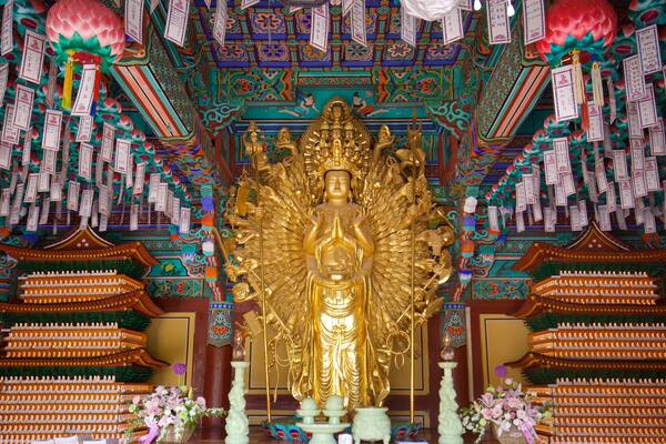 Une grande statue dorée dans un temple, ornée de décorations murales complexes et de nombreux drapeaux de prières.