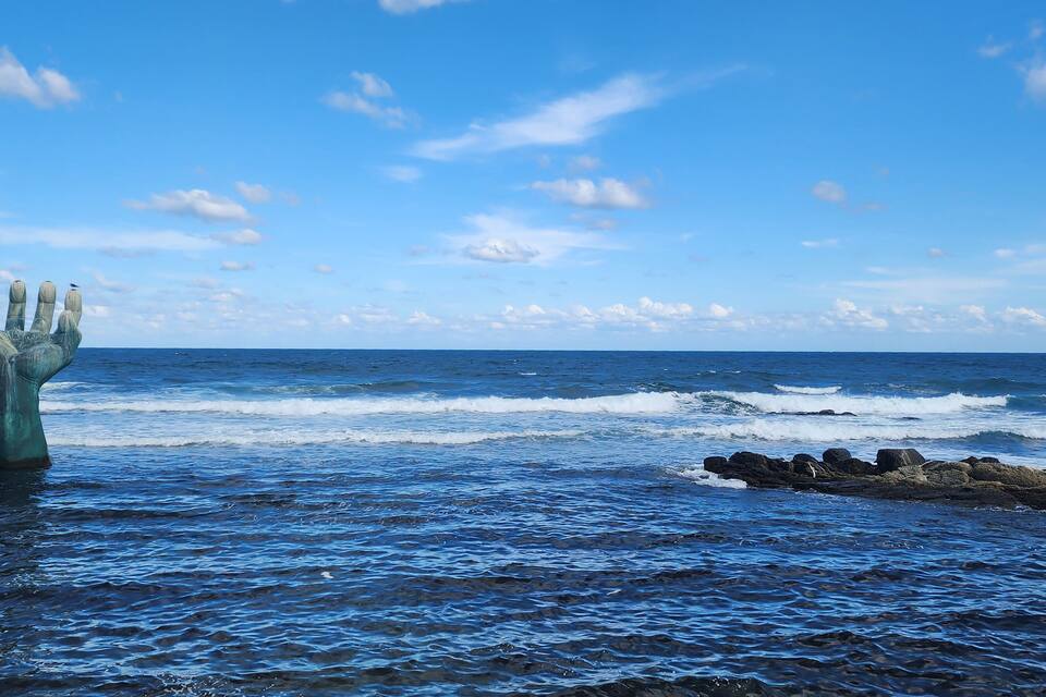Una escultura de mano en el océano, con olas y cielo despejado.