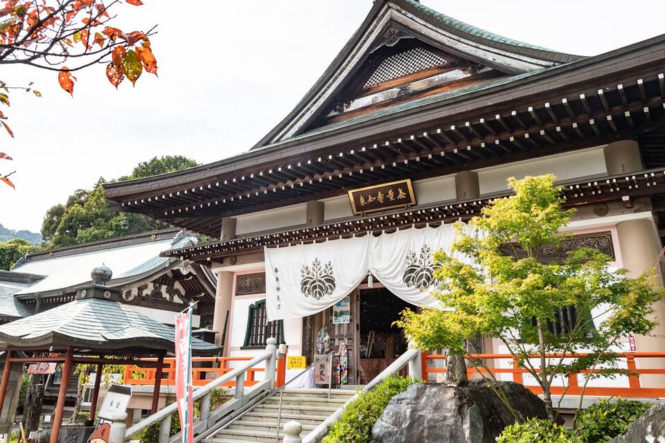 A traditional Japanese temple with a curved roof, white decorative banners, and a stone lantern.