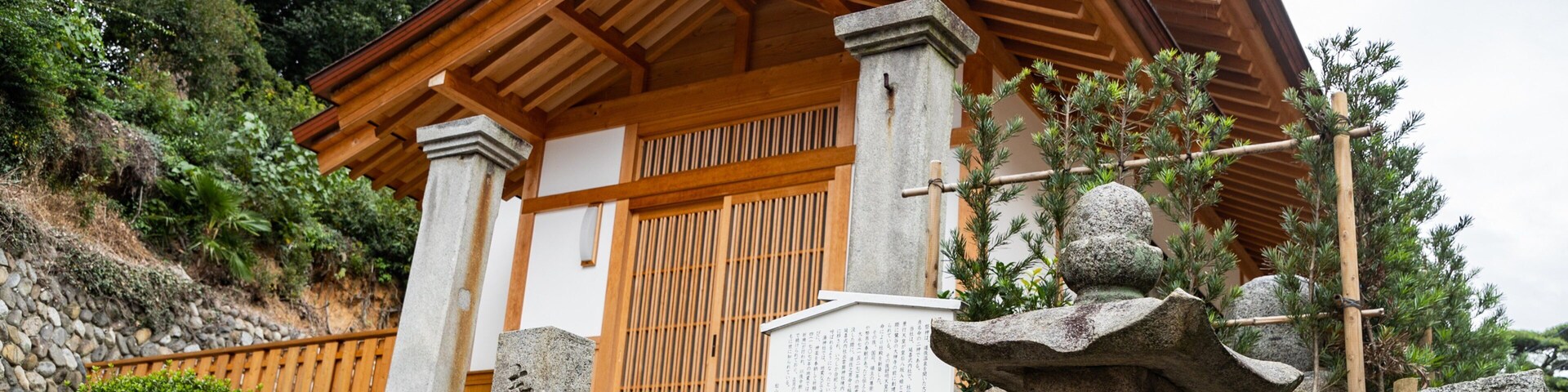 Um edifício japonês tradicional com fachada de madeira, pilares de pedra e um candeeiro de pedra.