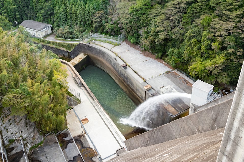 A dam with a water spillway, surrounded by dense forest.