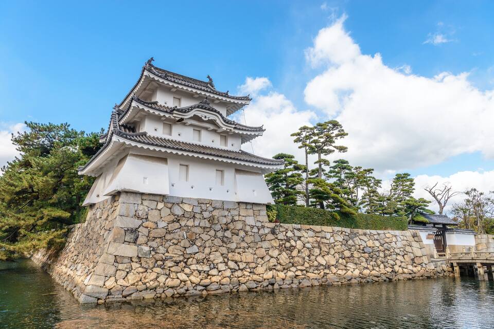 A traditional Japanese castle with a stone wall and a wooden bridge over a body of water.