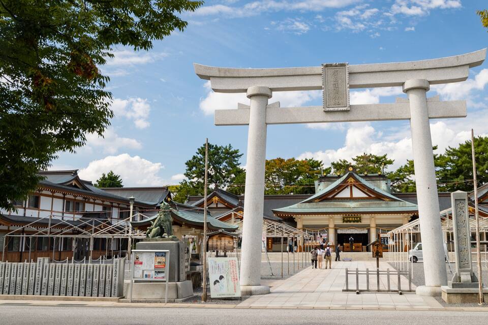 A traditional Japanese torii gate at the entrance of a shrine, surrounded by wooden buildings and trees.