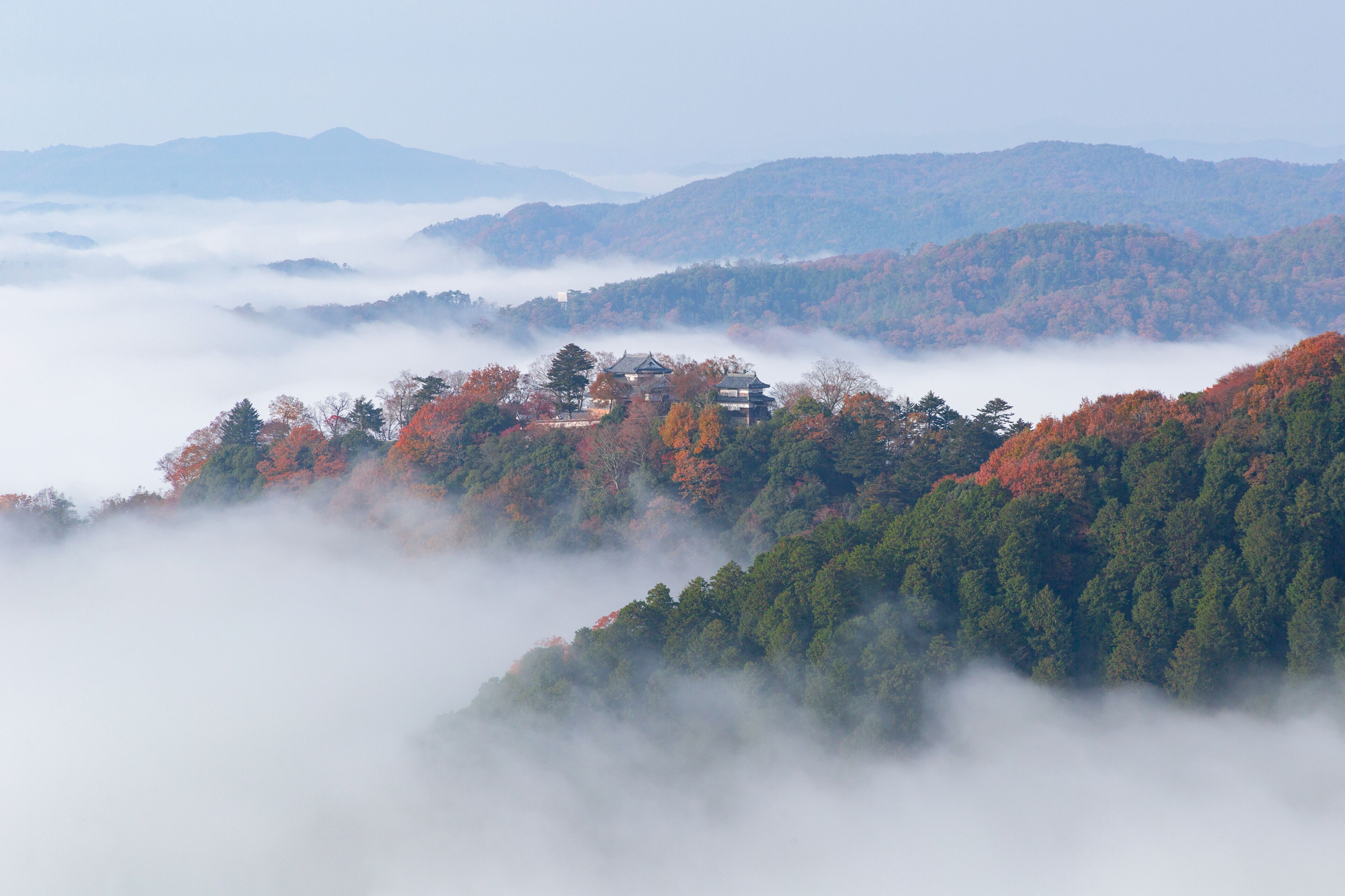 A mountainous landscape with autumn foliage and a traditional building nestled among the trees.