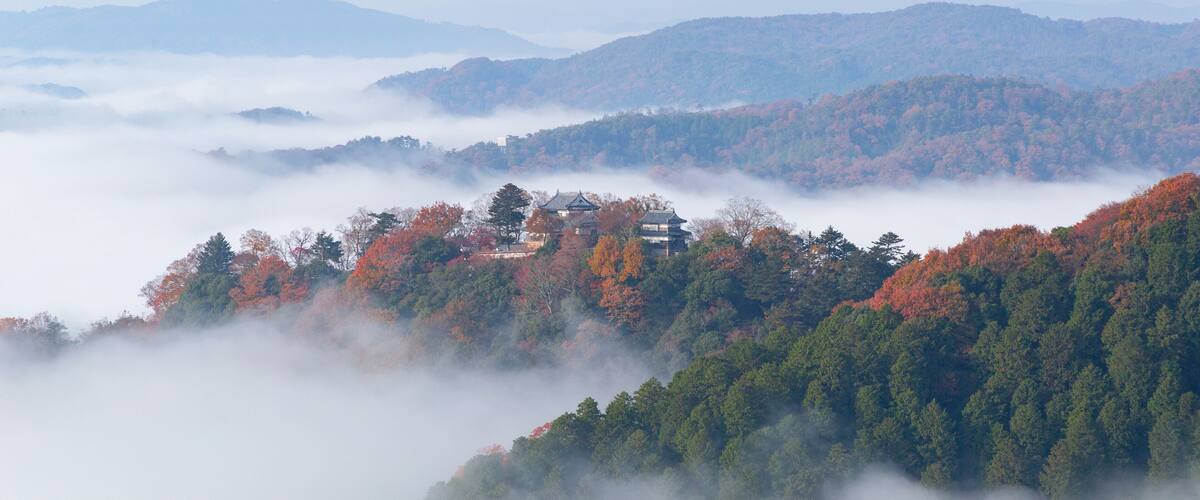 A mountainous landscape with autumn foliage and a traditional building nestled among the trees.