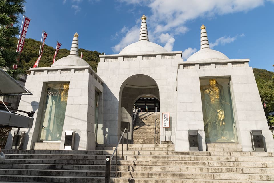A temple with three domes, a statue, and steps leading up to it.