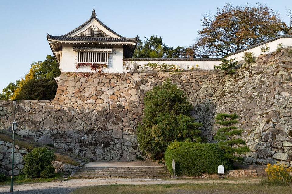 Ein traditionelles japanisches Gebäude mit einem Ziegeldach und einer Steinwand.