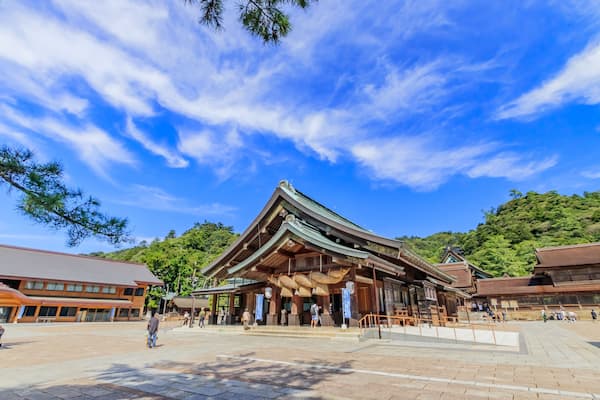 A traditional Japanese building with a tiled roof, surrounded by a paved area and trees.