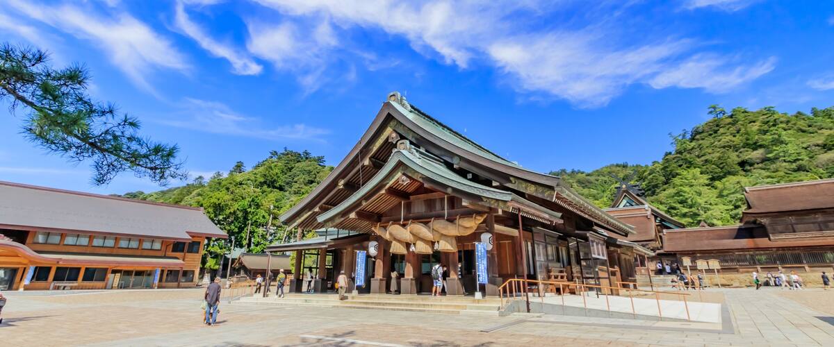 A traditional Japanese building with a tiled roof, surrounded by a paved area and trees.