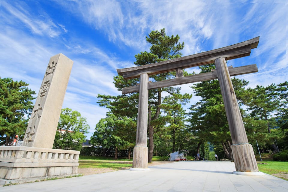 A traditional Japanese torii gate in a park with a stone monument and trees in the background.