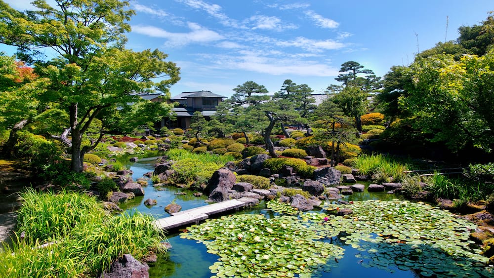 Ein friedlicher Garten mit Teich, Steinen und traditioneller japanischer Architektur im Hintergrund.