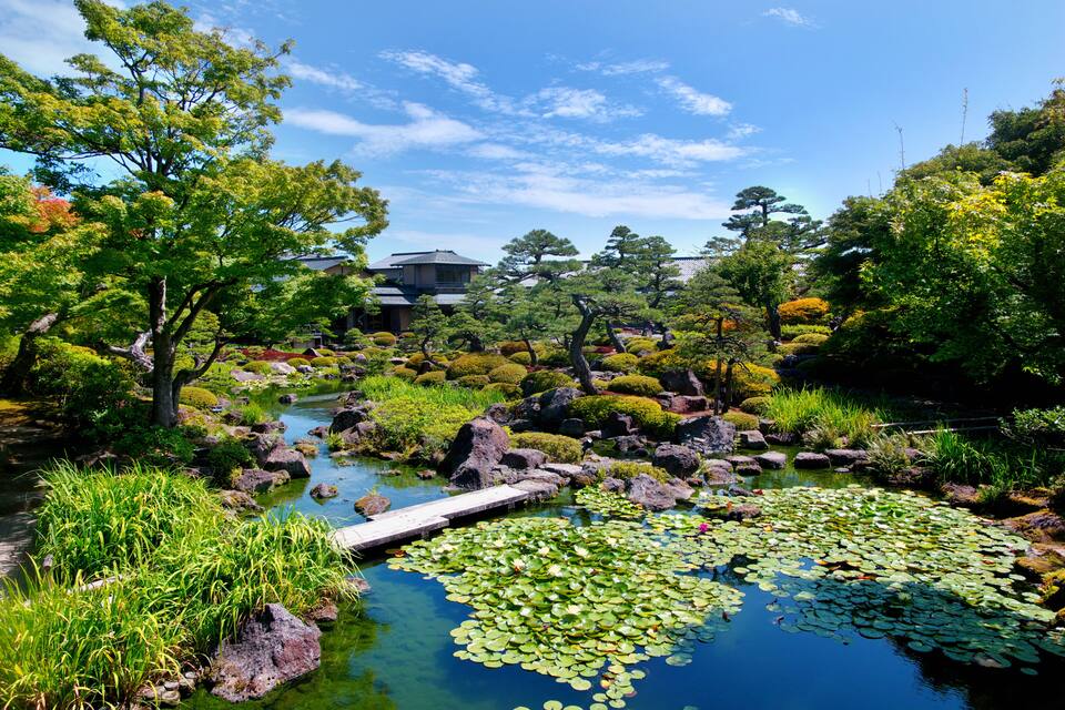 A serene garden with a pond, rocks, and traditional Japanese architecture in the background.