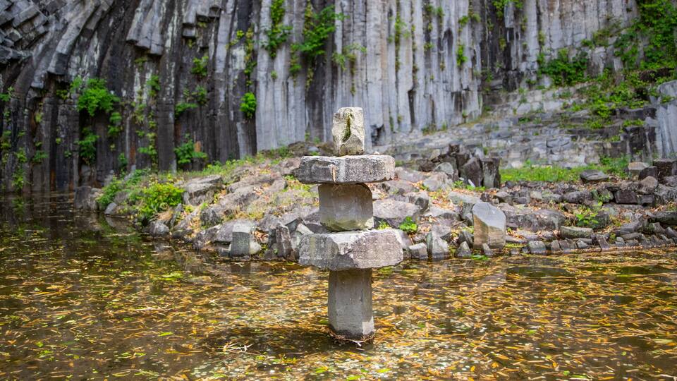A stone structure in a body of water with a rocky cliff in the background.