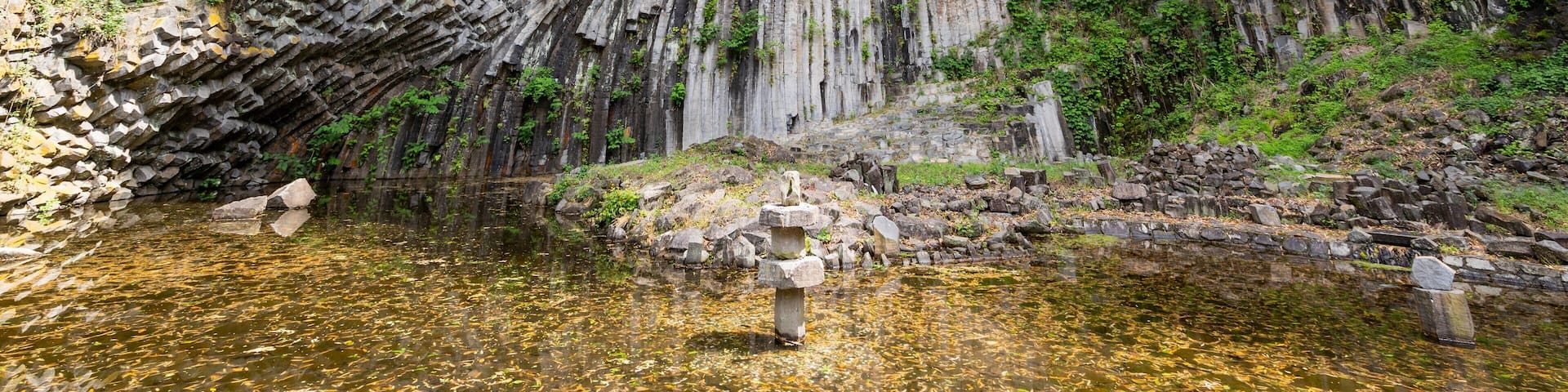 A waterfall cascading down a rocky cliff into a clear pool surrounded by lush greenery.