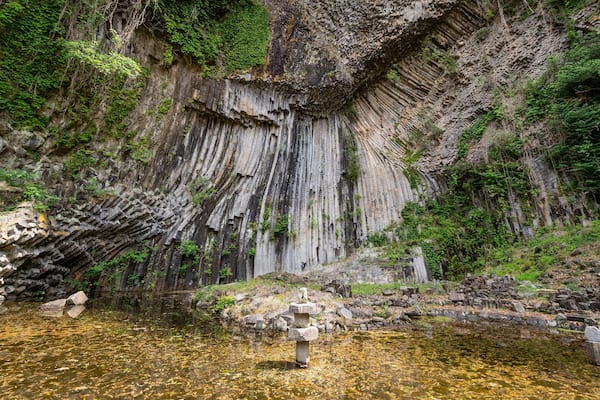 Une cascade se précipite le long d’une falaise rocheuse pour se déverser dans un bassin limpide, le tout étant entouré d’une végétation luxuriante.