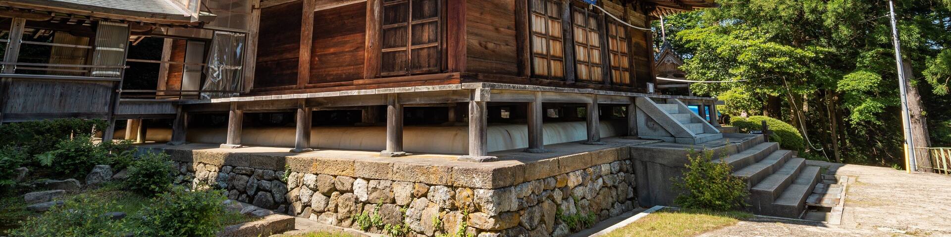 A traditional wooden building with a steeply pitched roof, surrounded by lush greenery and trees.