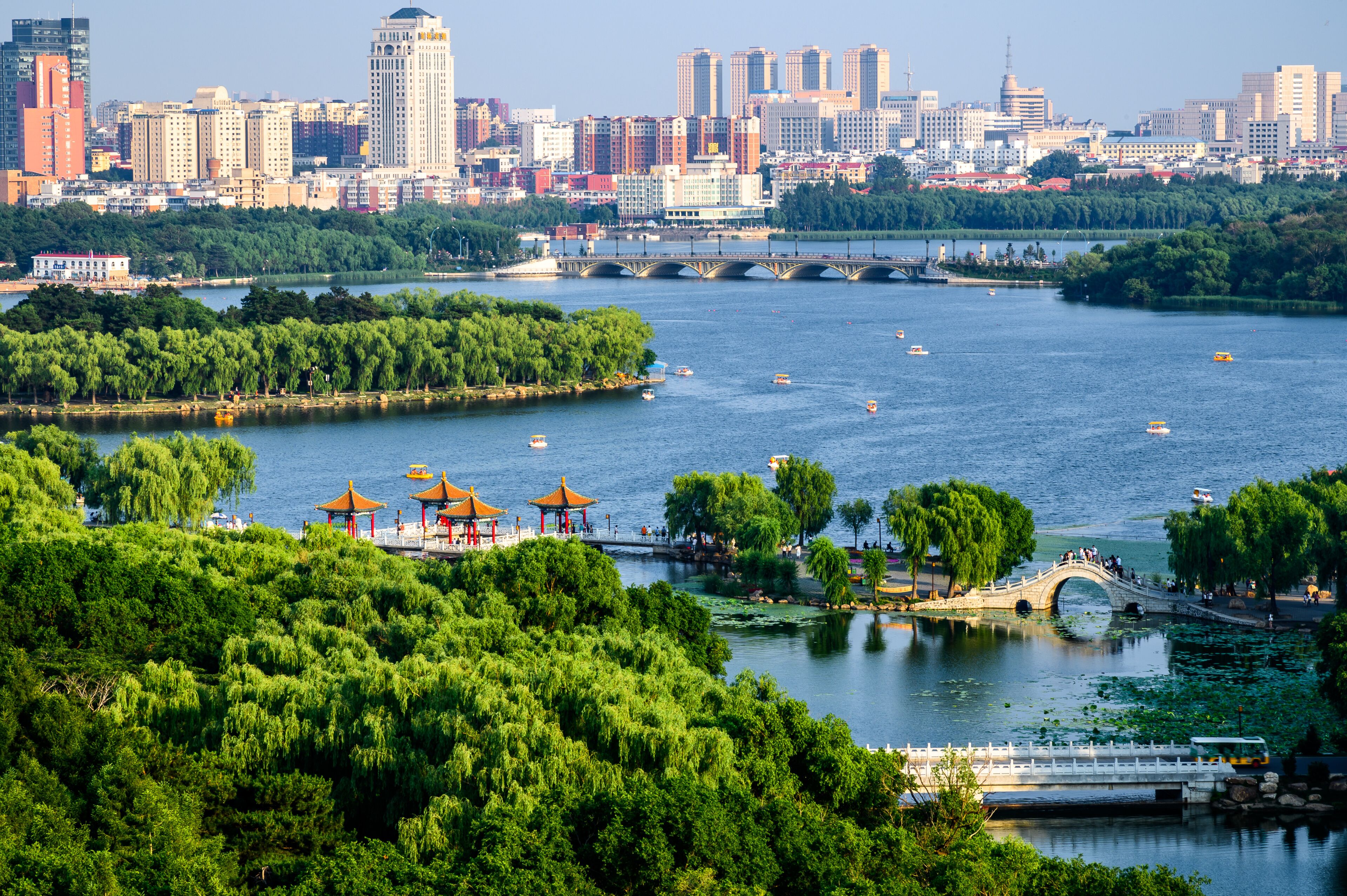 A river with boats, a bridge, a city skyline, and a park with pagodas.